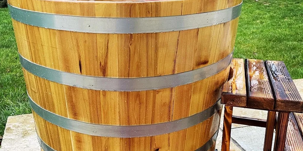 A wooden barrel-style cold tub in a garden, water steaming in cold morning air